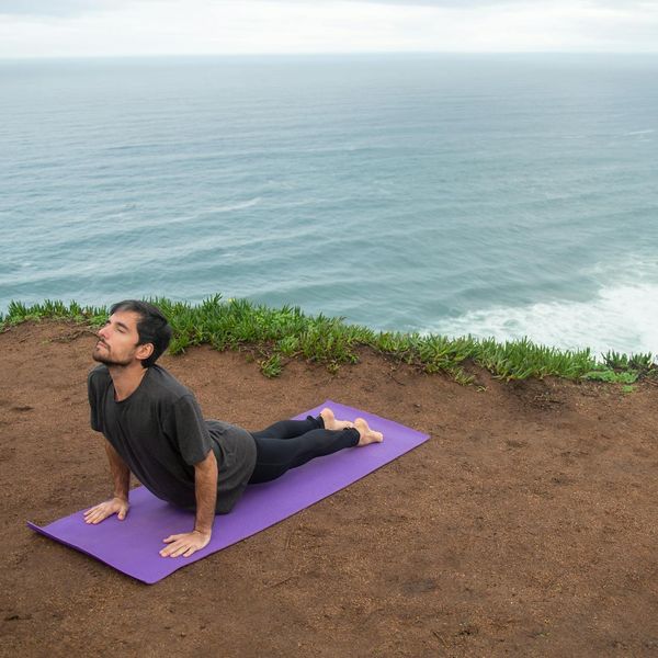 Man in a powerful warrior yoga pose on a cliff overlooking the sea.